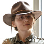 A headshot of a white middle aged woman wearing a big brown hat.