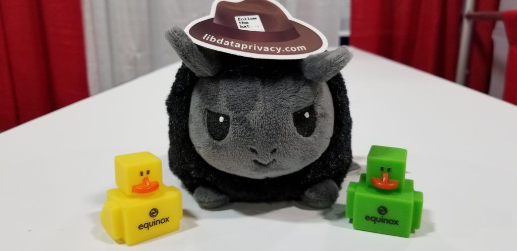 A black plushie llama flanked by two blocky yellow and green rubber duckies. The llama has a sticker of a brown hat on top of their head. Text on the hat: "follow the hat, libdataprivacy.com"