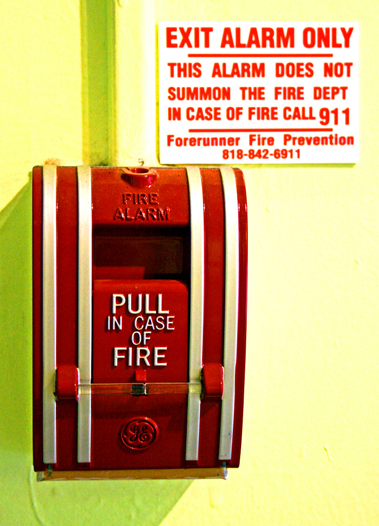 A pull fire alarm with a sign next to it stating "Exit Alarm Only - this alarm does not summon the fire dept In case of Fire call 911"