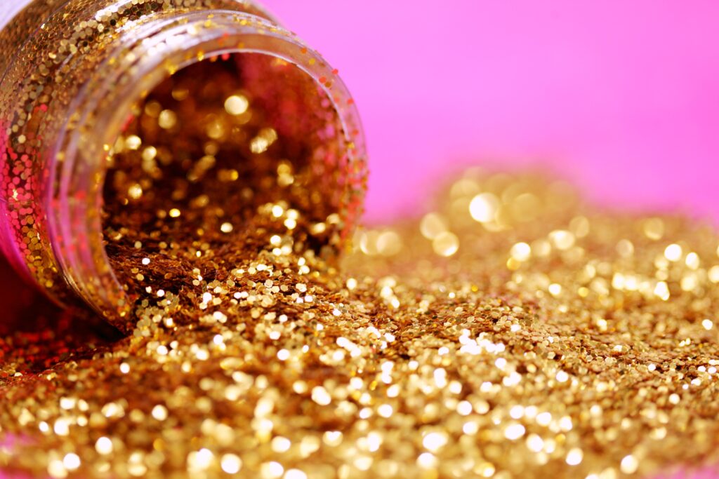 A container of gold glitter spilling over a flat pink surface.